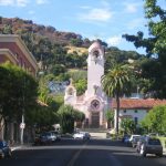 Mission San Rafael Arcángel with pink façade, bell tower, palm trees, and hillside backdrop on a sunny day in downtown San Rafael, CA.